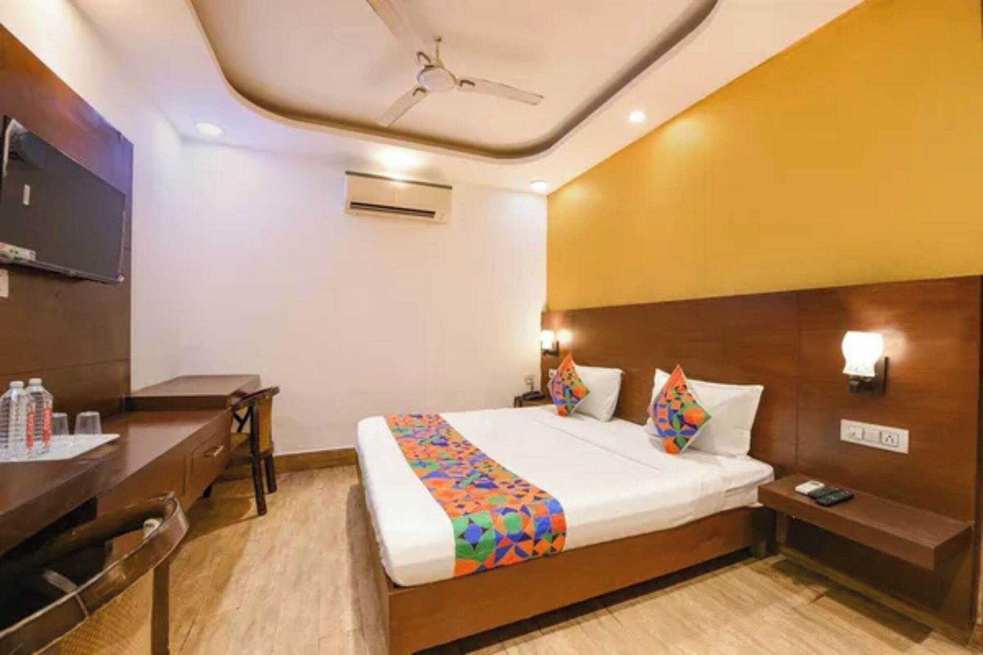 A hotel room with a bed, bedside table, nightstand, and a desk with a chair.