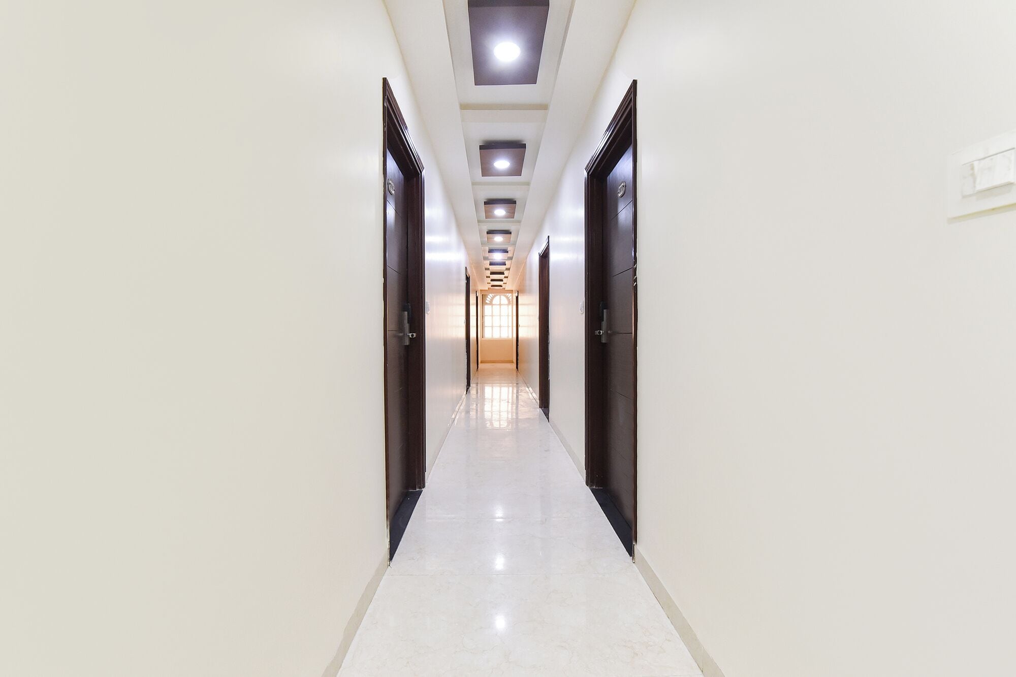 A long, narrow hallway with doors on both sides, leading to a bright room at the end.
