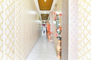 A corridor with patterned wallpaper, a tiled floor, and decorative vases with flowers. - Fabhotel Pacific View (Jaipur)