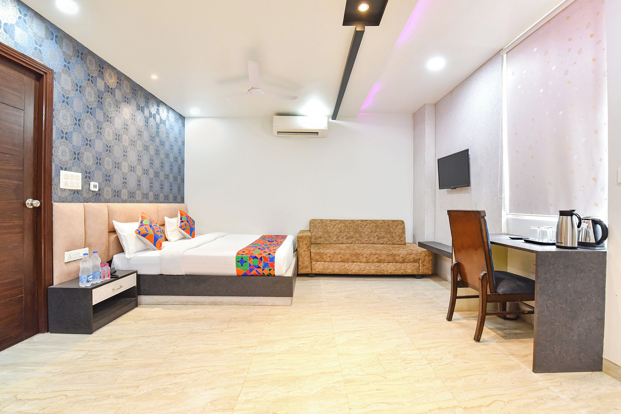 A hotel room with a bed, a sofa, a desk with a chair, a television, and a coffee maker.