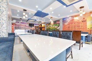 A restaurant with a long white table, blue cushioned seating, and murals of Indian architecture. - Fabhotel Pacific View (Jaipur)