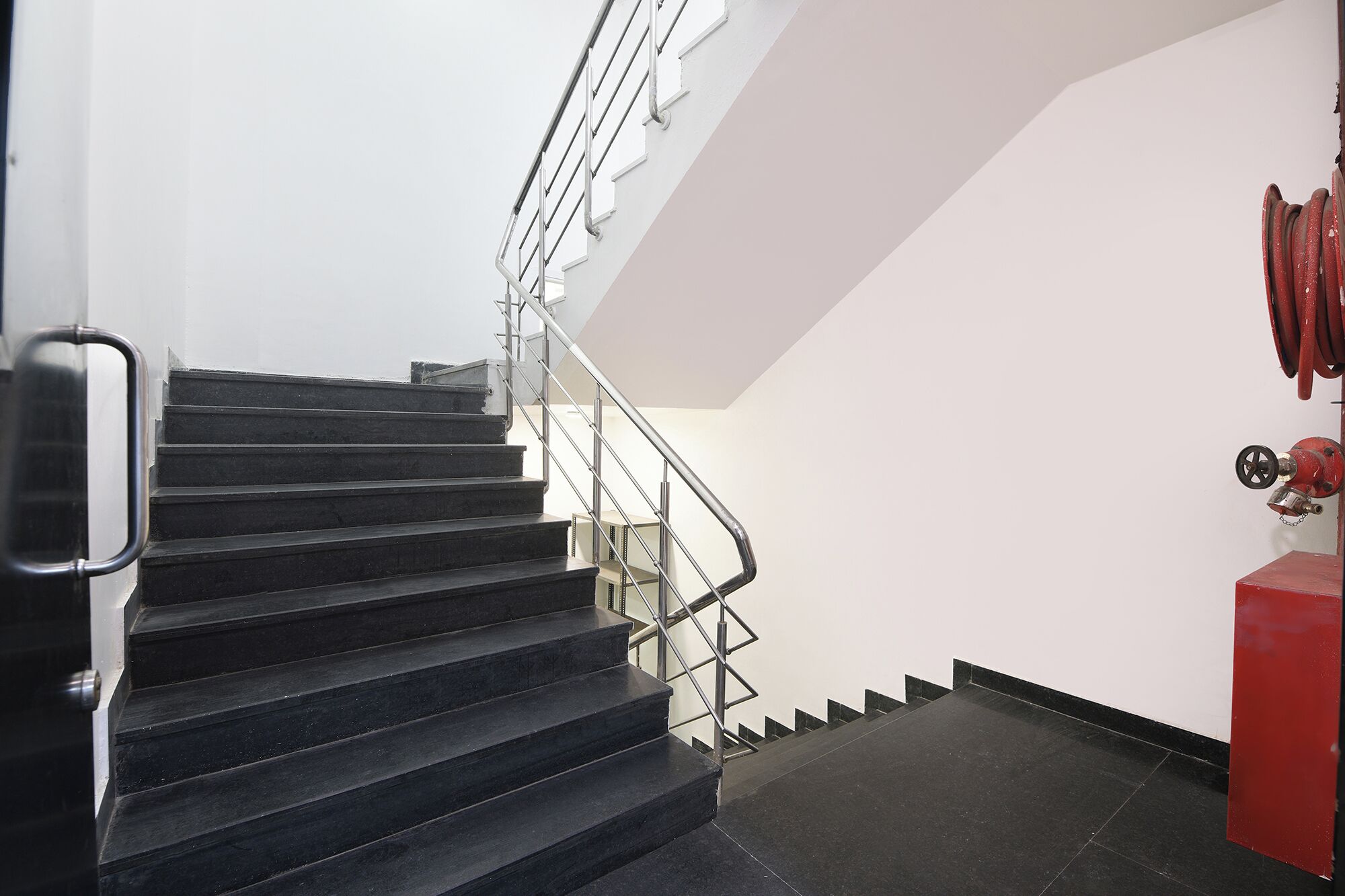 A staircase with metal railings and a red fire hose on the right.