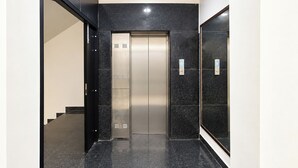 Een moderne lift met een metalen afwerking, gelegen in een hal met zwart marmeren wanden en een zwarte vloer.