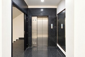 Um elevador moderno com acabamento metálico, situado em um corredor com paredes de mármore preto e piso preto.