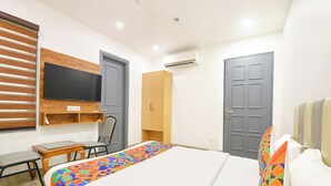 Een hotelkamer met een bed, een bureau, een stoel, een televisie en twee deuren.