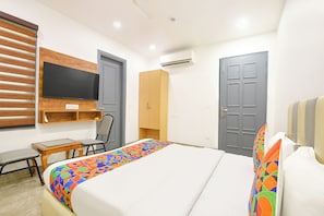 Quarto de hotel com cama, escrivaninha, cadeira, televisão e duas portas.