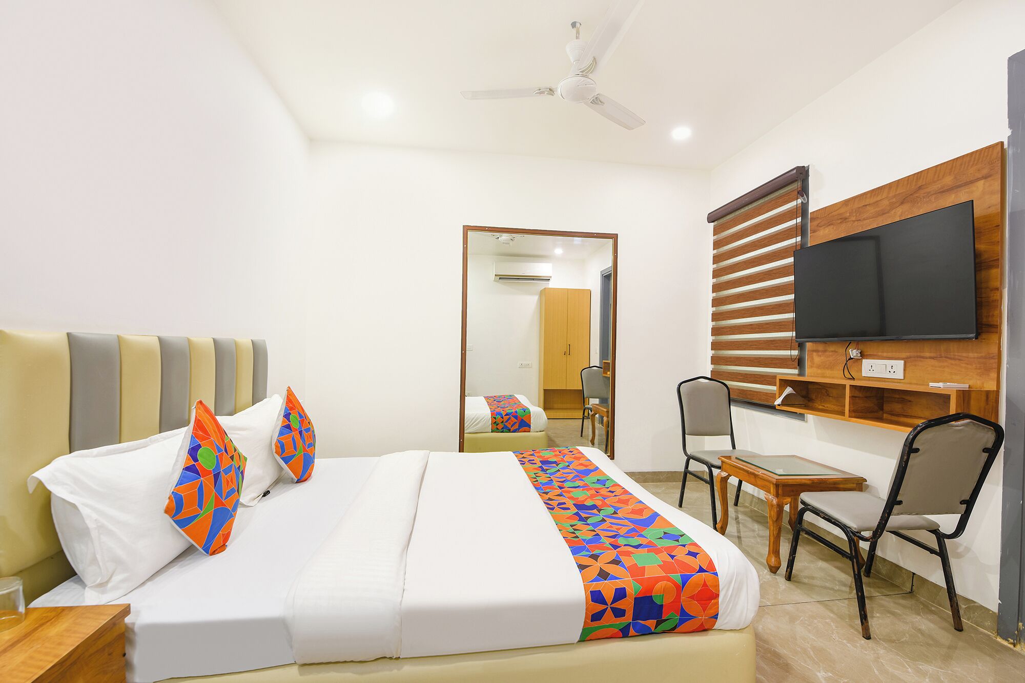 A hotel room with a bed, a desk, a chair, a television, and a ceiling fan.