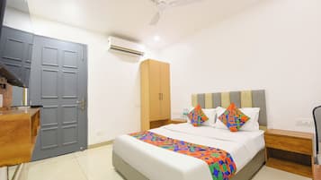 A hotel room with a bed, a desk, a wardrobe, a ceiling fan, and an air conditioning unit.
