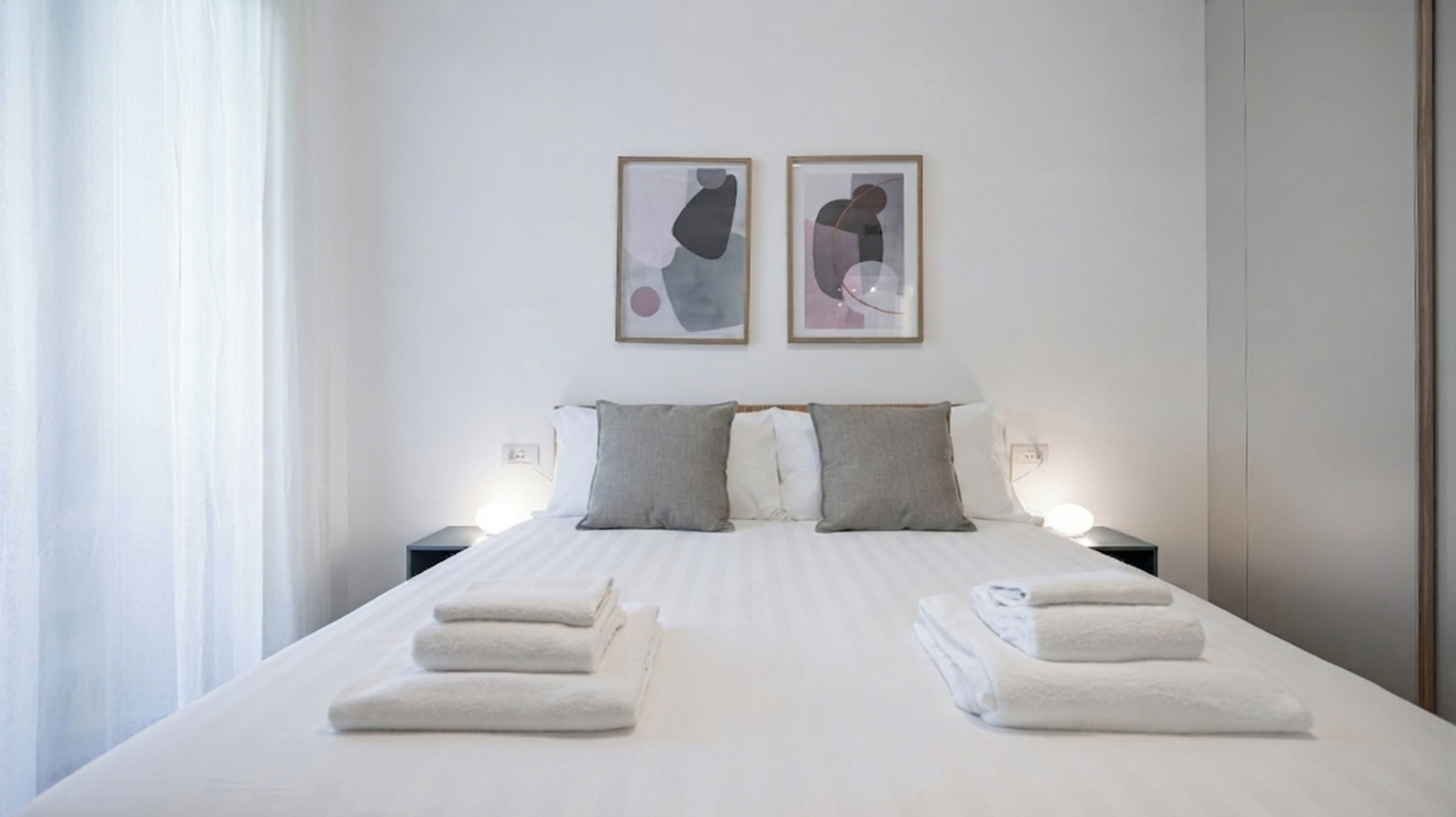 A hotel room with a neatly made bed, two bedside tables with lamps, and abstract artwork on the wall.