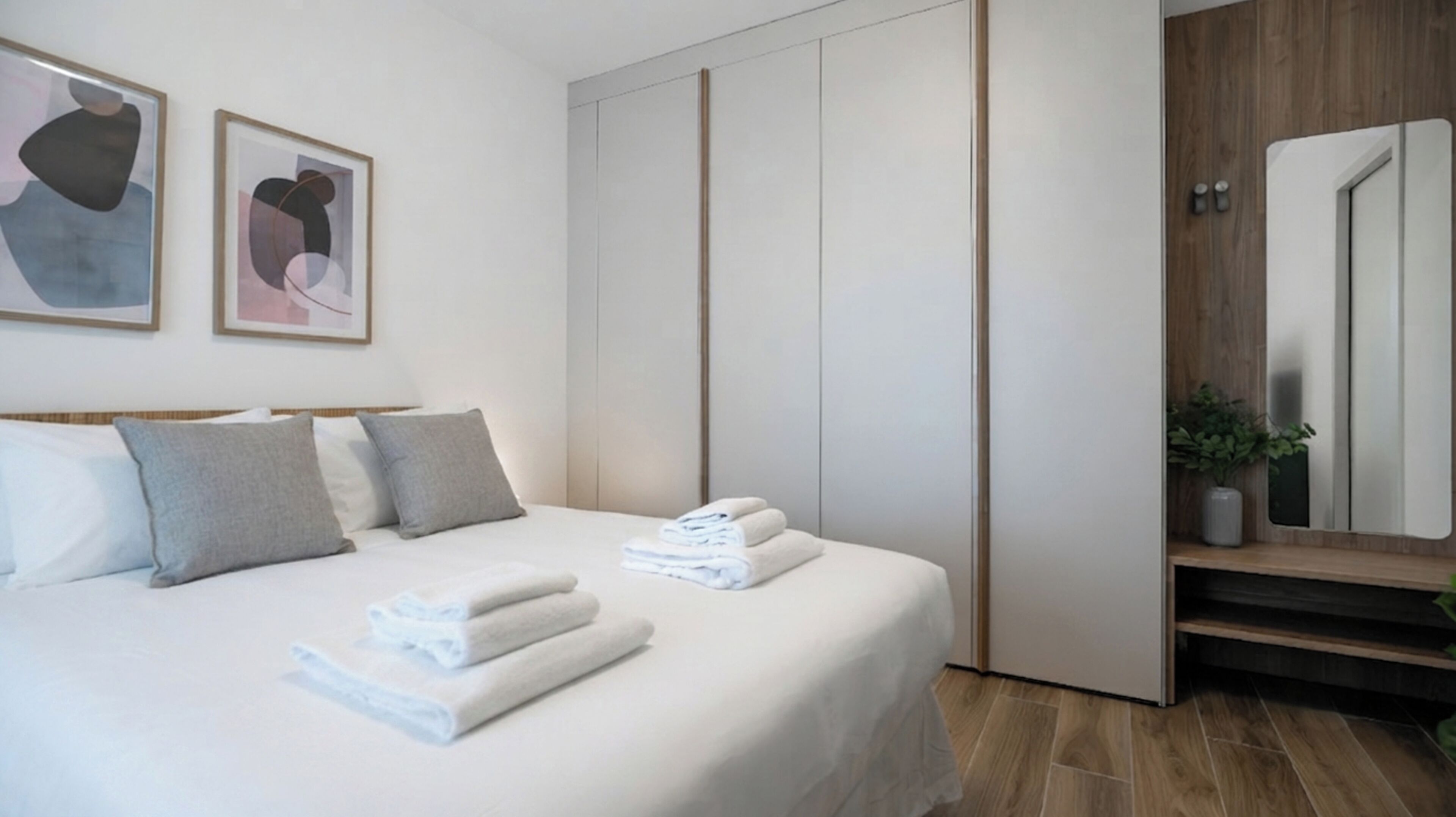 Una camera d'albergo moderna con un letto rifatto con cura, uno specchio grande e opere d'arte astratte alle pareti.