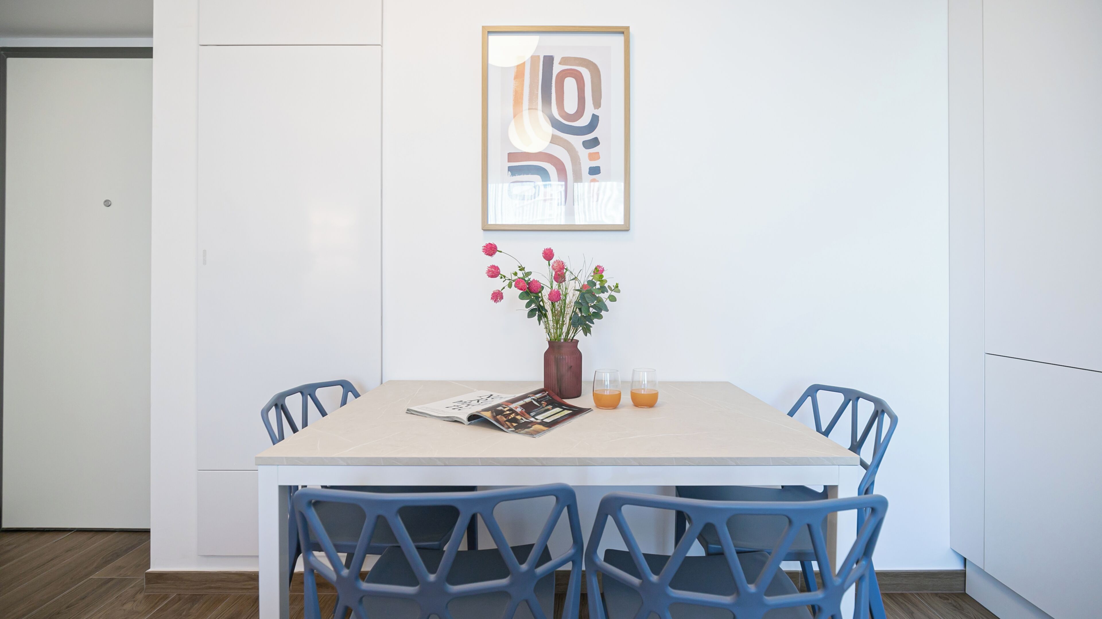 Ein Essbereich mit Tisch, Stühlen, einer Blumenvase und einem gerahmten Bild an der Wand.