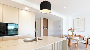 Et moderne køkken med en central ø, et spiseområde med stole og en hængende lampe.