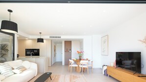 En moderne stue med sofa, sofabord, fjernsyn og spiseområde med stole og bord.