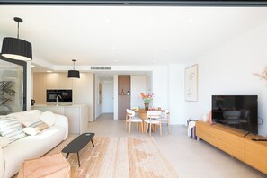 Ein modernes Wohnzimmer mit einer Couch, einem Couchtisch, einem Fernseher und einem Essbereich mit Stühlen und einem Tisch.