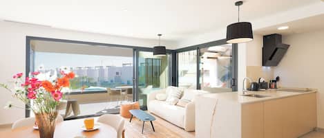A modern apartment with a dining area, a sofa, a kitchen, and large windows.