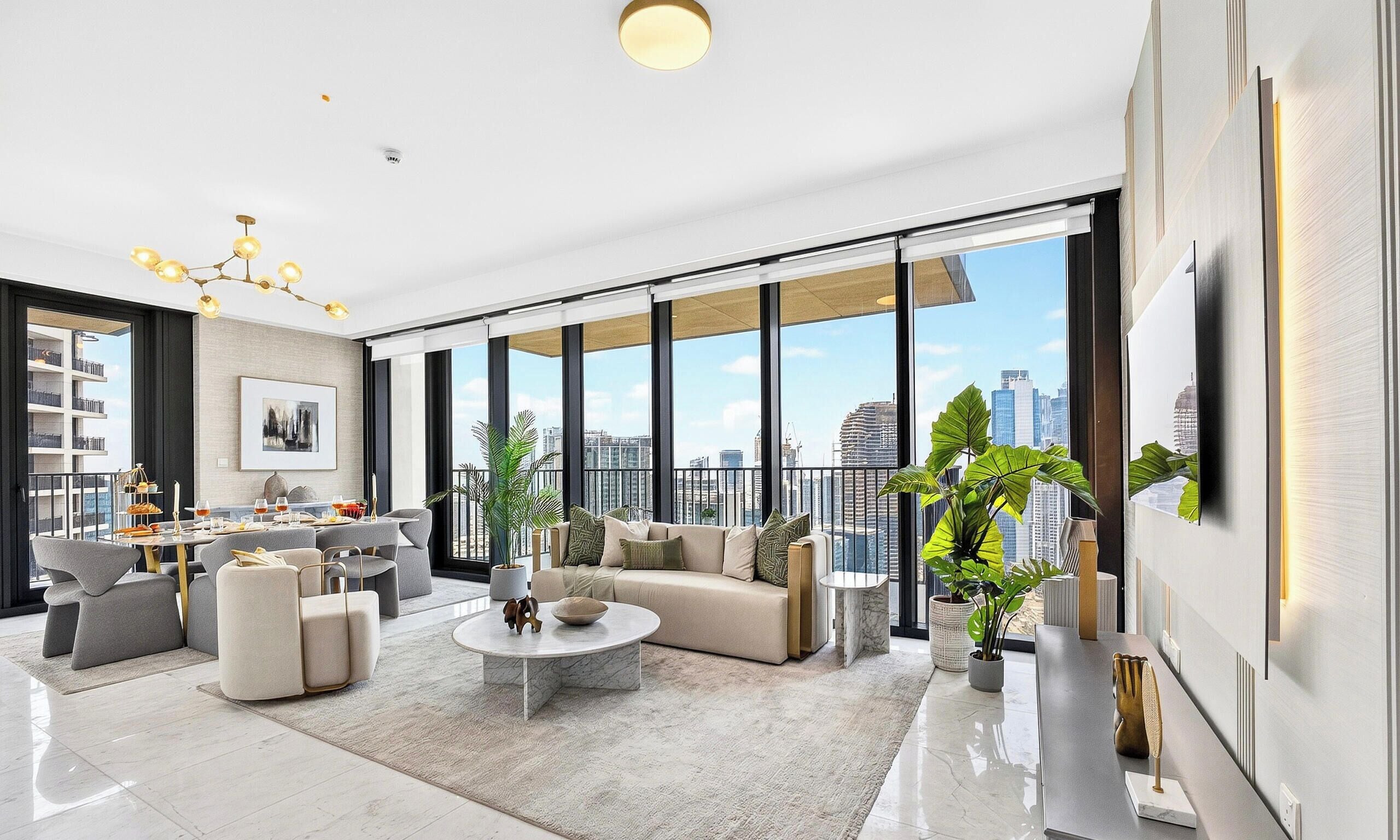 A spacious living room with a large window, a dining area, and a modern chandelier.