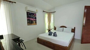 A hotel room with a bed, a desk, a chair, an air conditioner, a door, and a painting on the wall. - Chaya Village F Shared Pool & Jacuzzi (Ko Lanta)