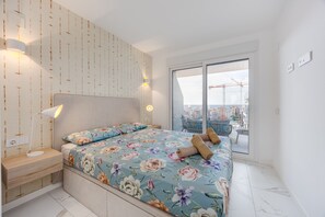 Een slaapkamer met een groot bed, een nachtkastje, een wandlamp en uitzicht op de stad door een schuifdeur.