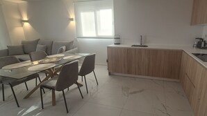 Een moderne keuken met een centraal eiland, een eethoek met een glazen tafel, en een raam dat voor natuurlijk licht zorgt.