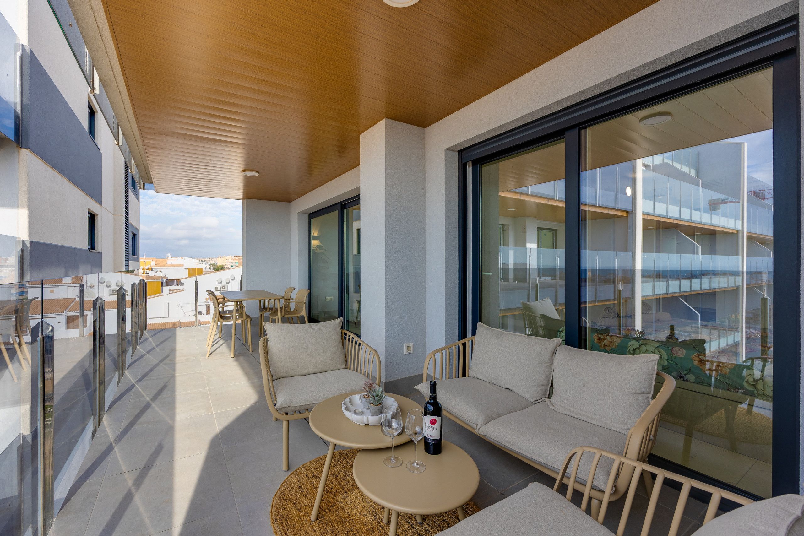 A modern outdoor seating area with a round table, chairs, and a sofa, overlooking a cityscape.