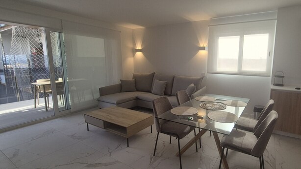 Een modern interieur met een glazen eettafel, zachte zitplaatsen, een keukenhoek en een schuifpui naar buiten.