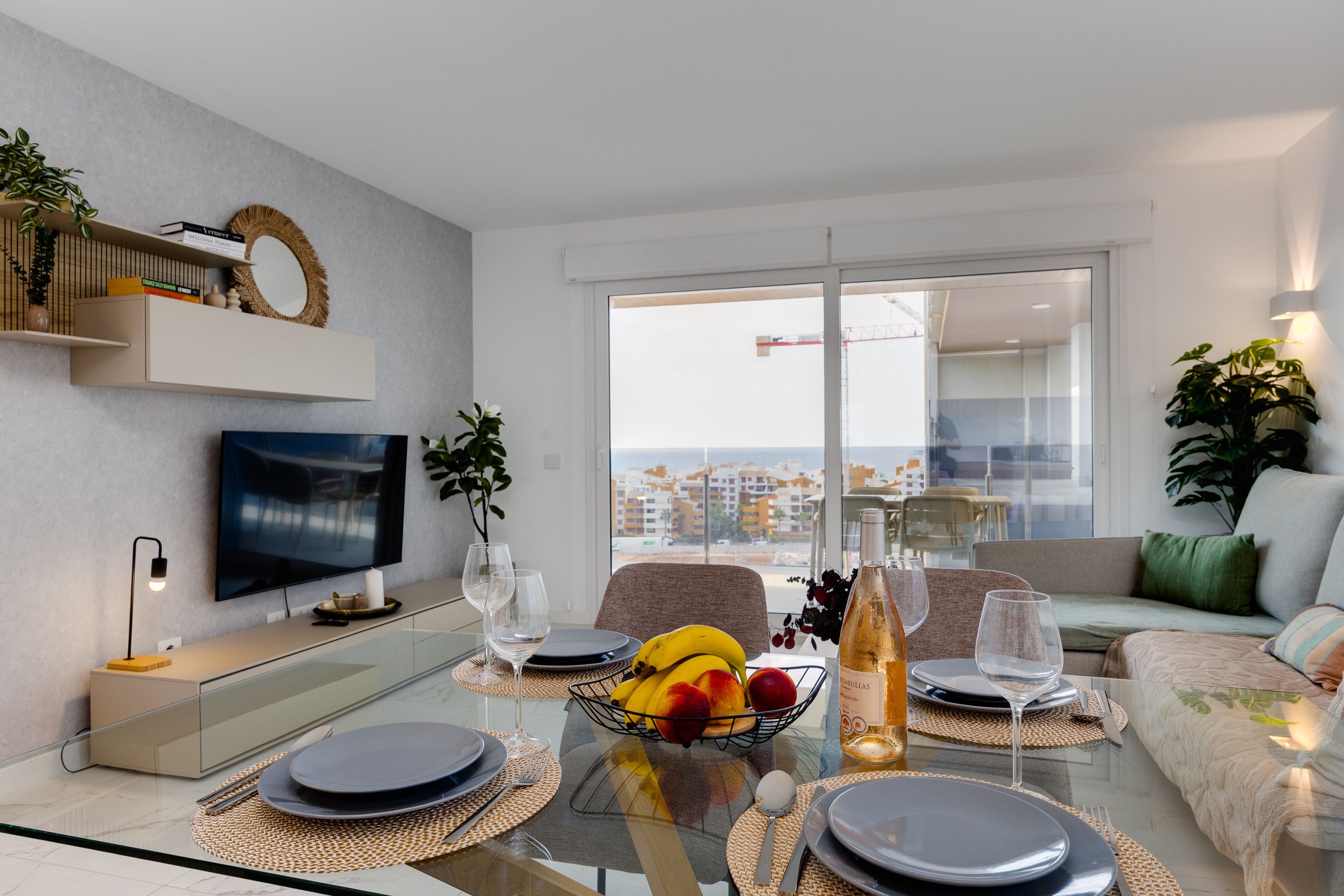 A modern living room with a dining area, a flat-screen TV, and a view of a construction site.