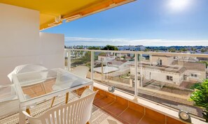 A balcony with a glass table and chairs, offering a view of buildings and greenery. - Apartment Santa Ana Villamartin (Orihuela Costa)