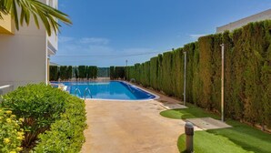 En swimmingpool med krystalklart vand, omgivet af en velplejet hæk, en støbt sti og et lille græsstykke.