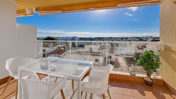 En balkon med et glasbord og stole, en potteplante og udsigt over bybilledet.