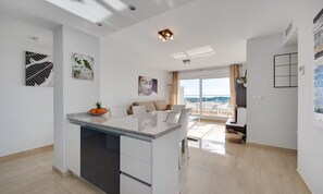 A modern kitchen with a central island, a dining area with a sofa, and a view of the outdoors. - Apartment Santa Ana Villamartin (Orihuela Costa)