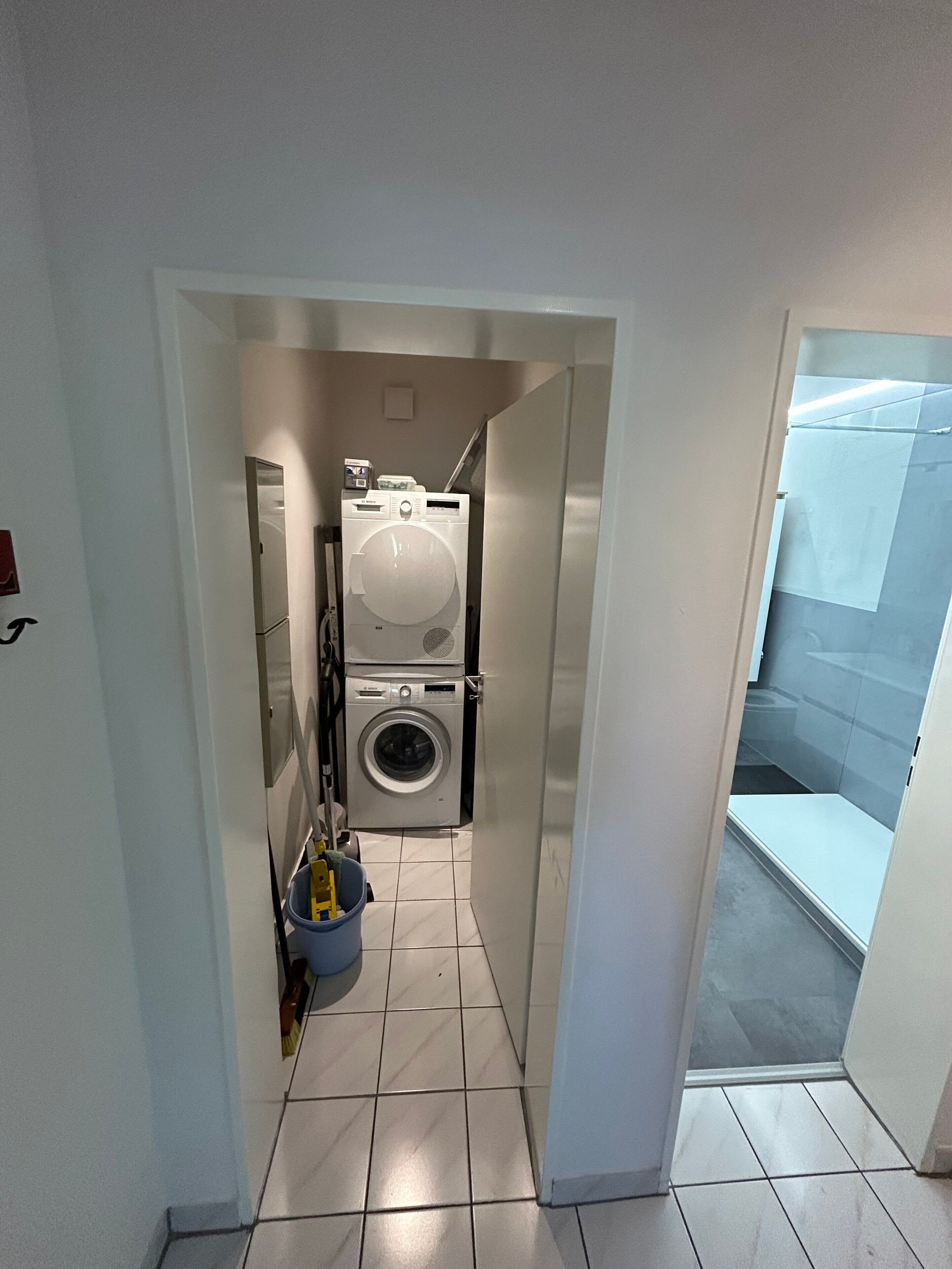 A compact laundry room with a washing machine and dryer, a small trash bin, and a tiled floor.