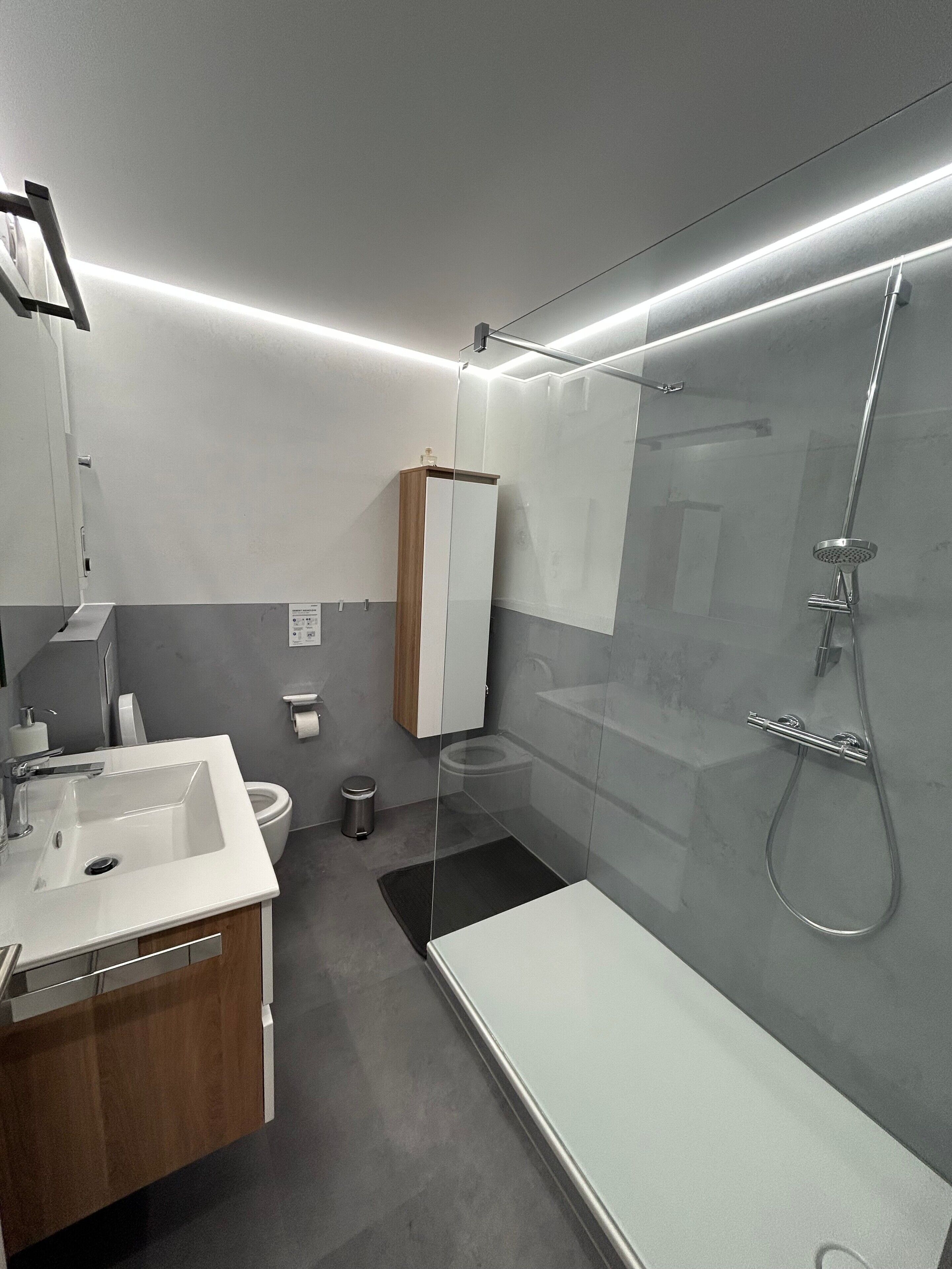 Un baño moderno con cabina de ducha de vidrio, lavamanos blanco y tocador de madera.