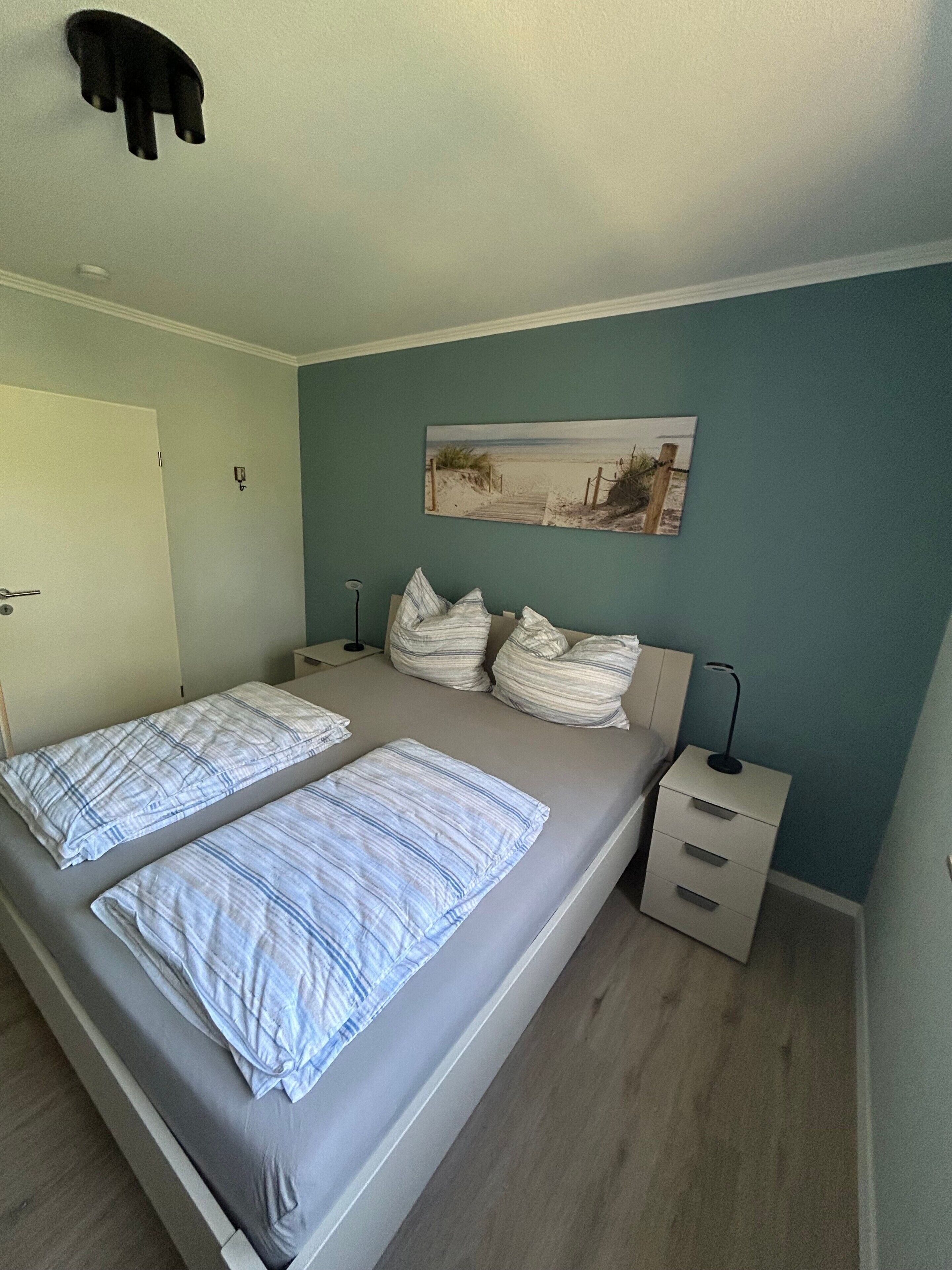 Een slaapkamer met twee bedden, een nachtkastje, een wandlamp en een schilderij met een strandthema.