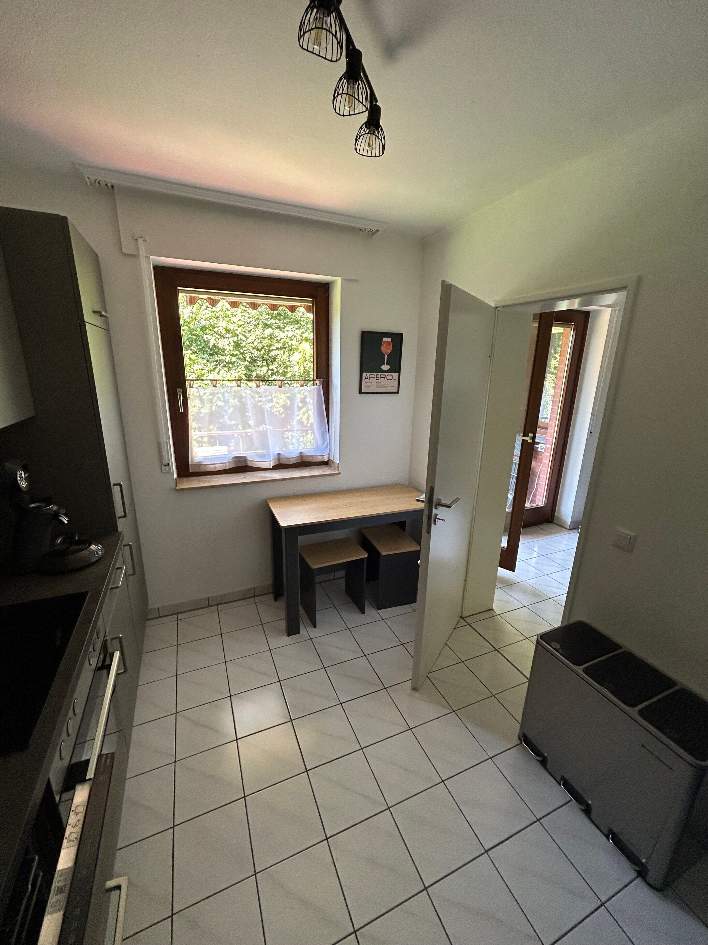 A kitchen with a window, a bench, and a trash bin.