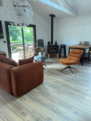 A modern living room with a large window, a black wood-burning stove, and a brown sofa. - Renovated chalet in Gère Belesten near Laruns with mountain views (Gere Belesten)