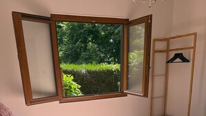 Een slaapkamer met een bed, een raam en een houten plank met kledinghangers.