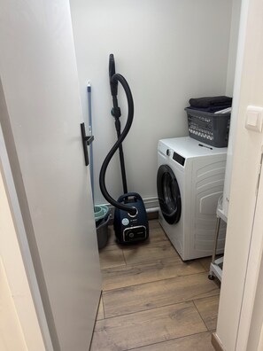 A laundry room with a washing machine, a vacuum cleaner, and a basket on the floor. - Renovated chalet in Gère Belesten near Laruns with mountain views (Gere Belesten)