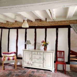 Ein Zimmer mit freiliegenden Holzbalken, einem weißen Schrank mit Schubladen, einem roten Sessel, einem Streifenstuhl und einer Vase mit Blumen.