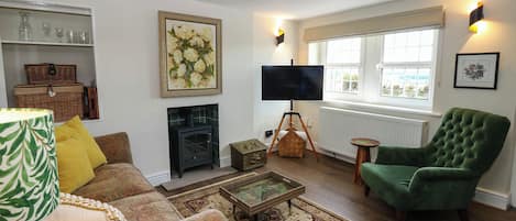 A living room with a sofa, a green armchair, a fireplace, a television, and a window with a view.