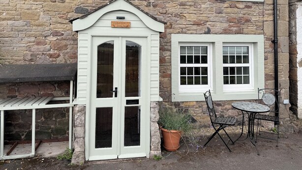 Edificio de piedra con puerta y ventanas blancas, un pequeño espacio de estar al aire libre y un letrero que dice 'Ashcroft'.