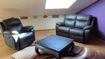 Een kamer met twee leren fauteuils, een houten bijzettafeltje en een schuin dak met dakraam.