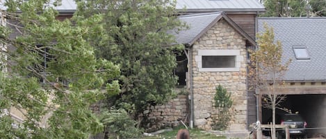 A stone building with a sloped roof, surrounded by trees and a fenced area with horses.