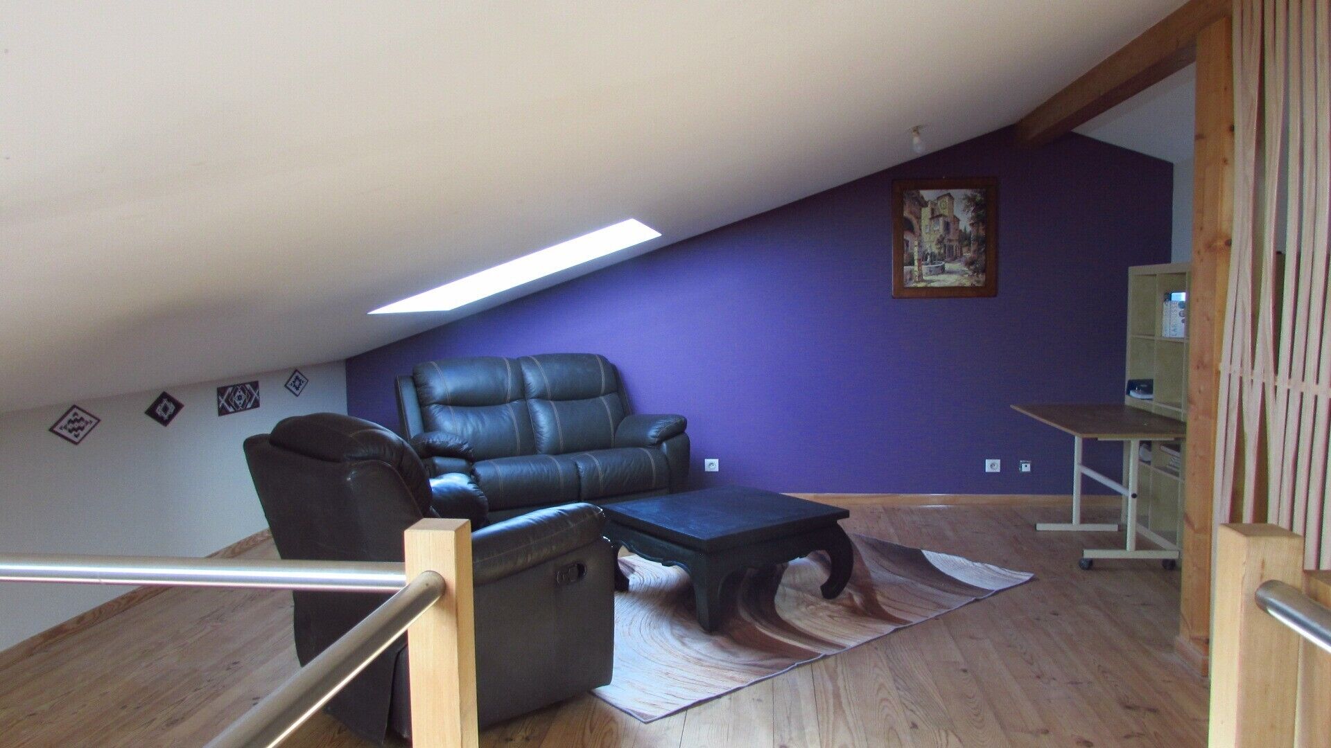 Ein Zimmer mit schrägem Dach, einem schwarzen Ledersessel, einem kleinen Tisch und einer violetten Wand.