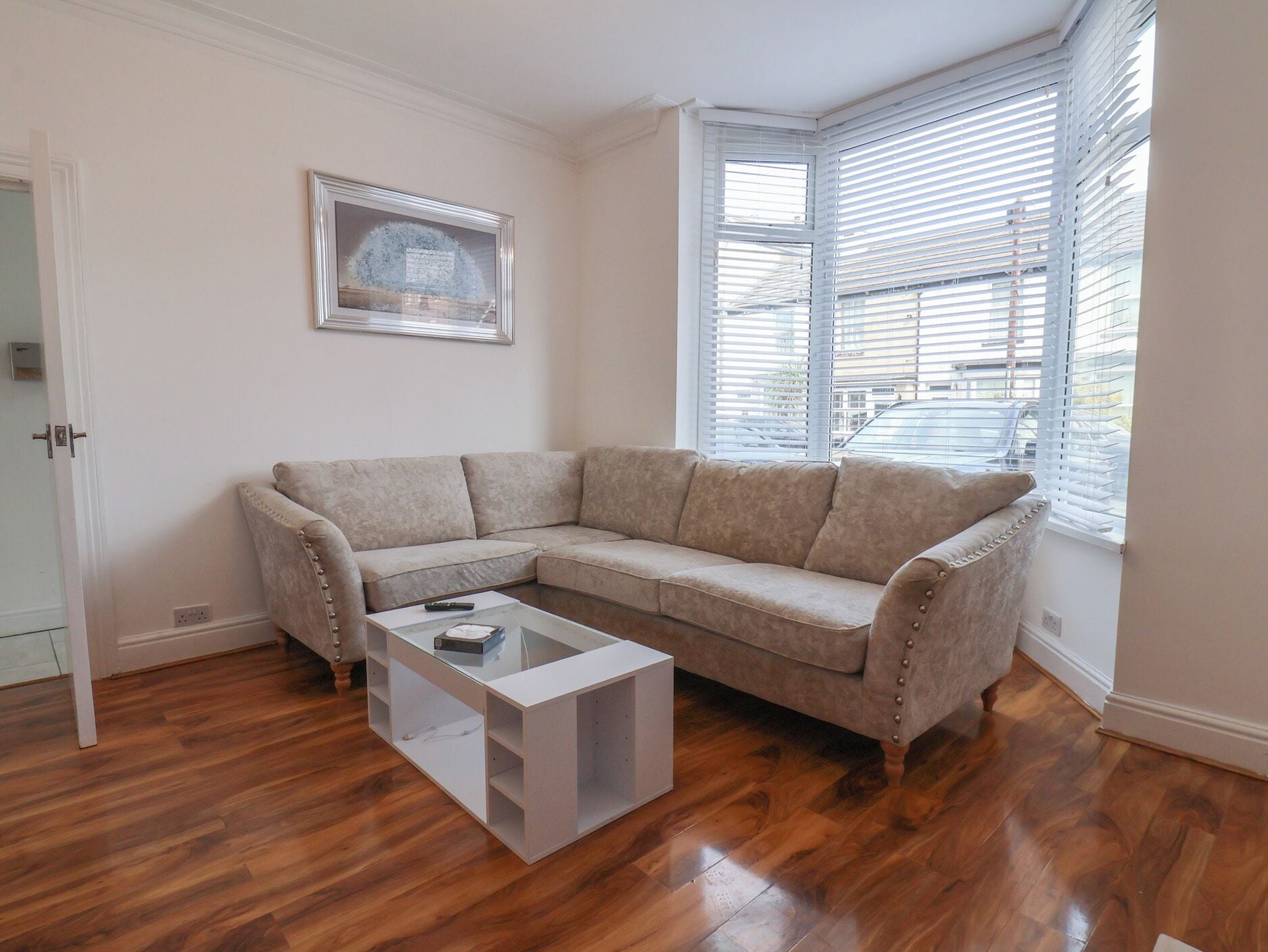 A living room with a beige sectional sofa, a glass coffee table, and a framed picture on the wall.