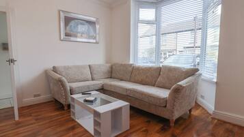 Una sala de estar con un sofá seccional color beige, una mesa de centro de vidrio y un cuadro en la pared.