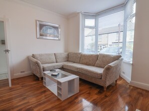 Una sala de estar con un sofá seccional color beige, una mesa de centro de vidrio y un cuadro en la pared.