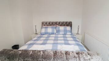 Un dormitorio con cama, mesita de noche, lámpara y radiador.