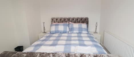 A bedroom with a bed, a nightstand, a lamp, and a radiator.