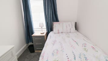 Um quarto com uma cama, uma mesa de cabeceira, uma luminária e uma janela com cortinas.