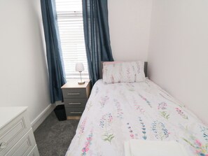 Un dormitorio con cama, mesita de noche, lámpara y ventana con cortinas.